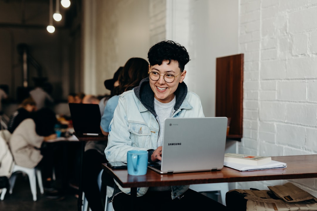 Smiling man sitting and using samsung laptop near people