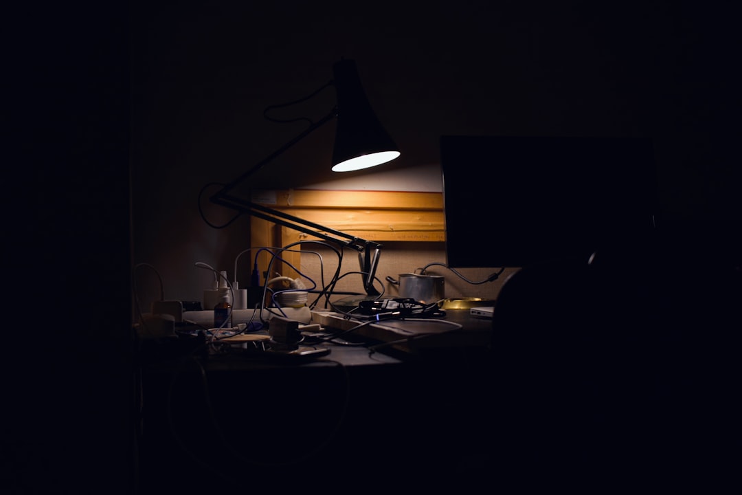 A dark room with a desk lamp and a computer