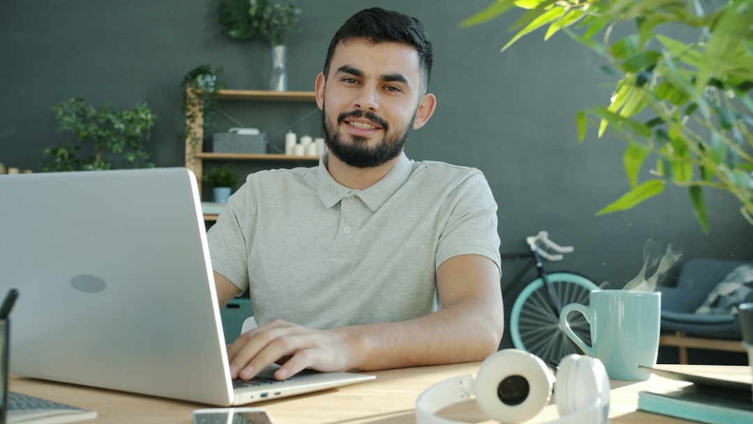 A man smiles while working on a laptop.